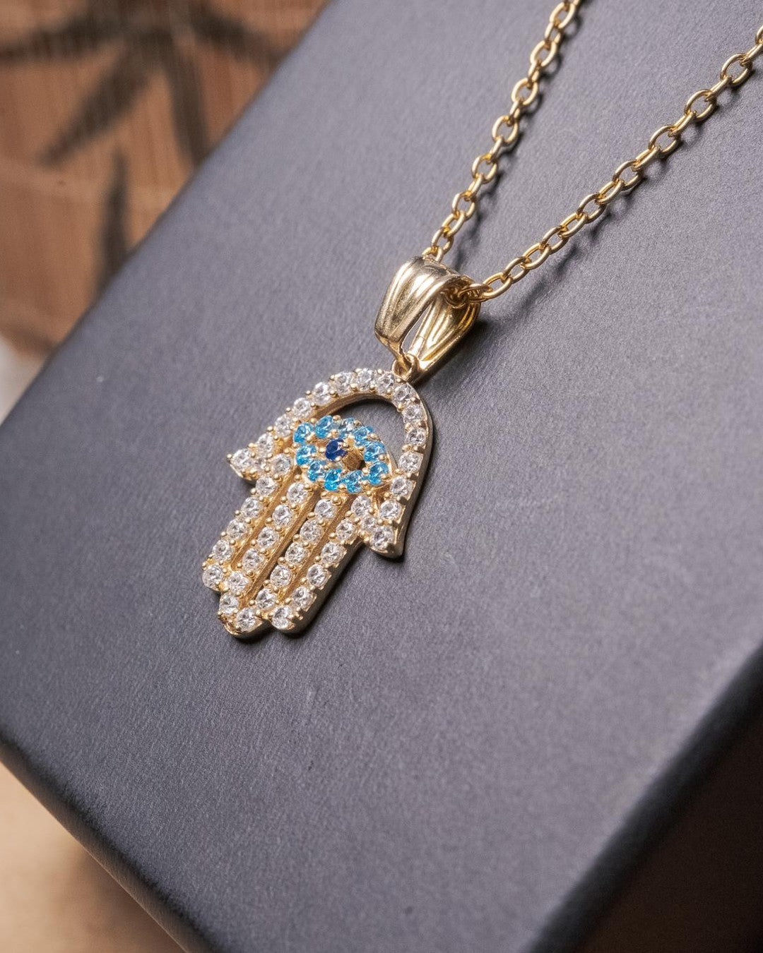 Pingente mão de fátima em ouro amarelo com safiras brancas e azuis.