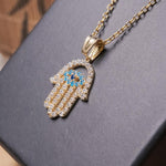 Pingente mão de fátima em ouro amarelo com safiras brancas e azuis.