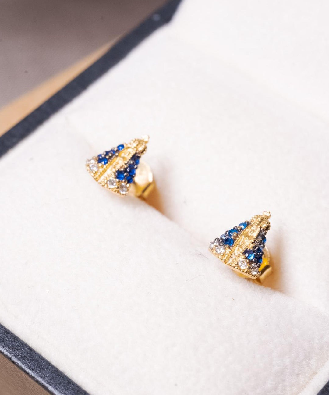 Brincos Stud de Nossa Senhora Aparecida em ouro amarelo com safiras azuis e brancas.