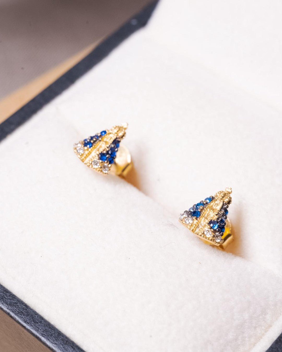 Brincos Stud de Nossa Senhora Aparecida em ouro amarelo com safiras azuis e brancas.