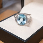 Anel em ouro branco com topázio azul oval de 1.2cm e diamantes brilhantes.