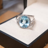 Anel em ouro branco com topázio azul oval de 1.2cm e diamantes brilhantes.