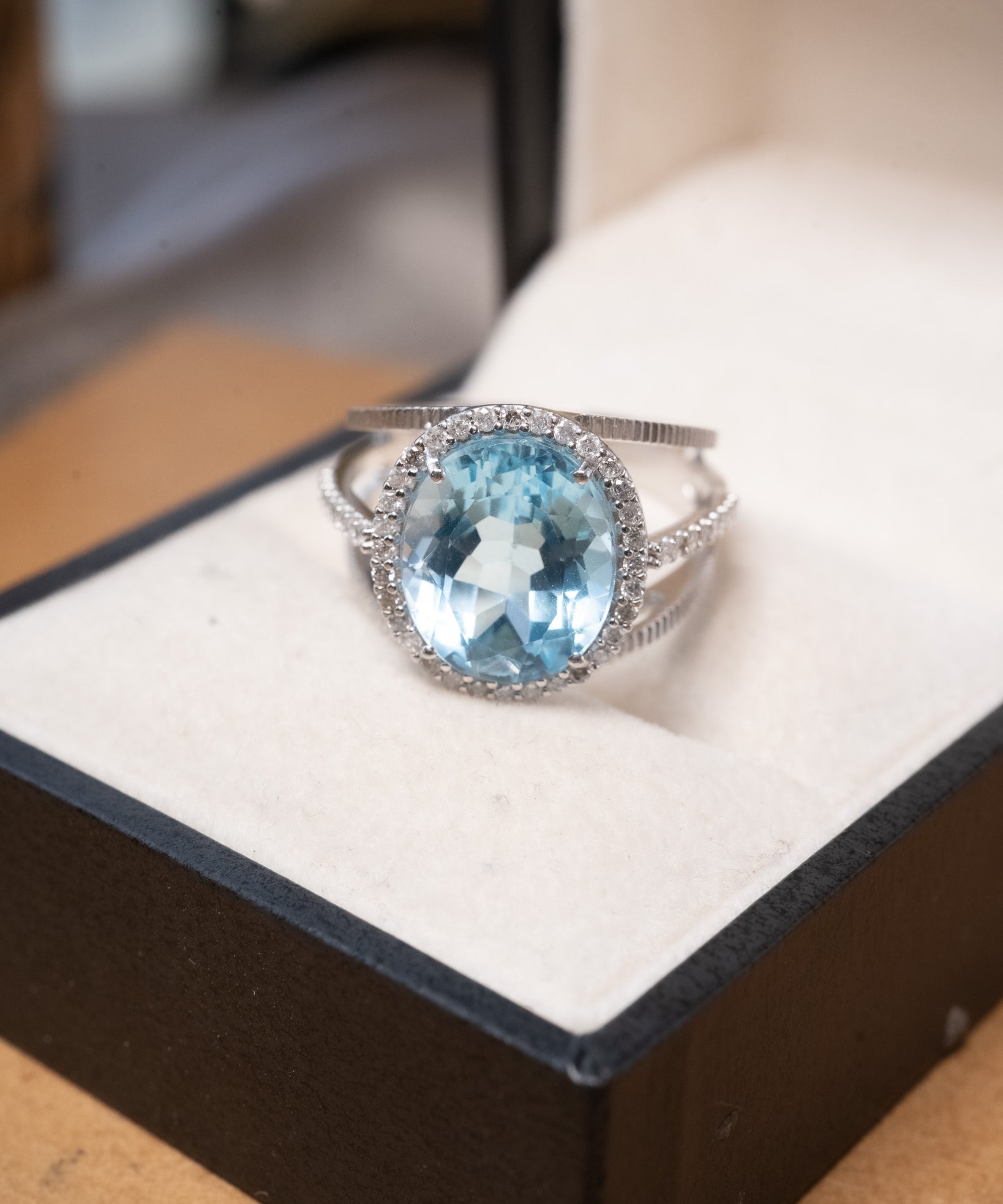 Anel em ouro branco com topázio azul oval de 1.2cm e diamantes brilhantes.